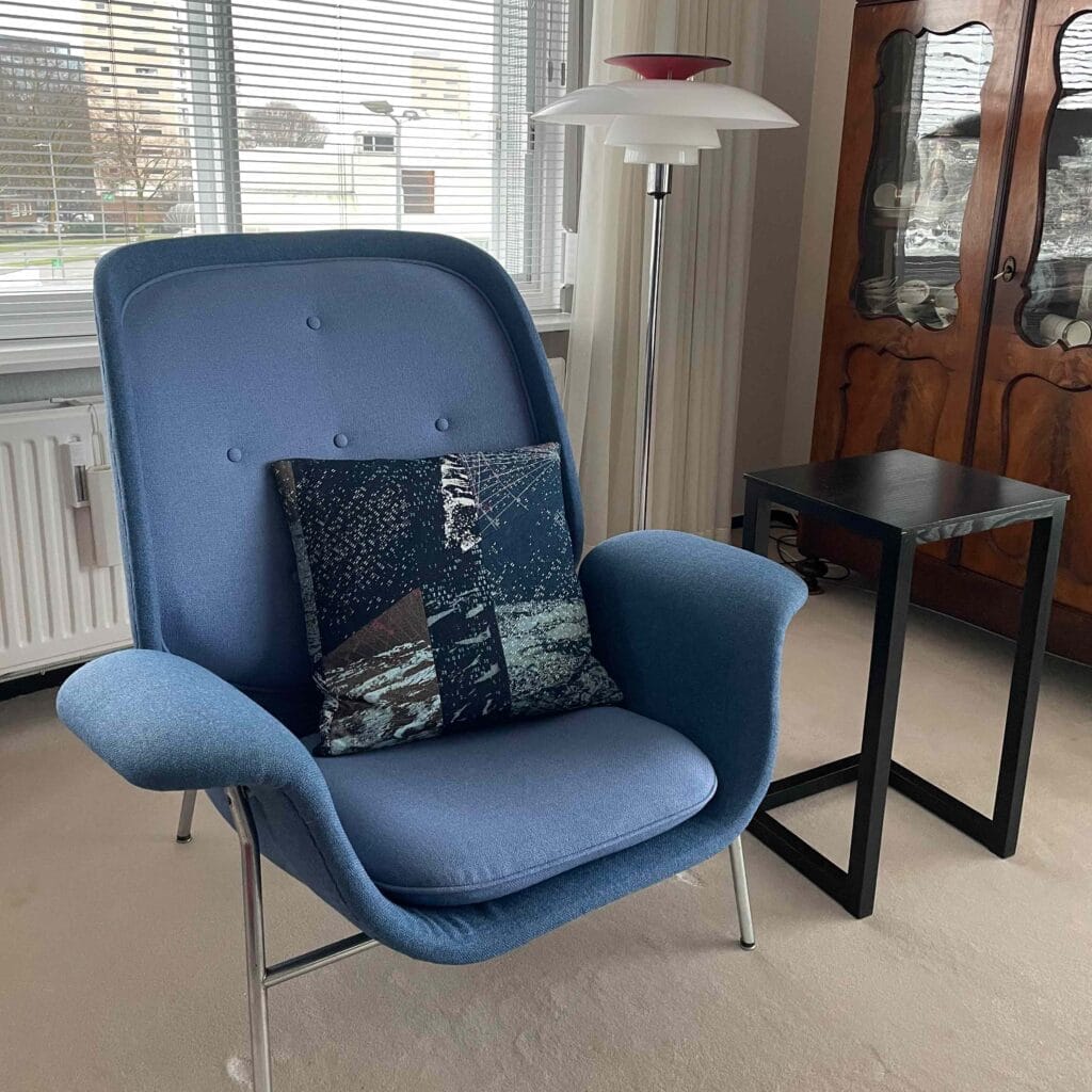 View of a Space Collection large pillow by MIN-studio on a blue chair. The pillows are screen-printed denim with layered moon surface textures in blue, grey, and neon pink inks, featuring edgy, grunge-inspired abstract patterns.