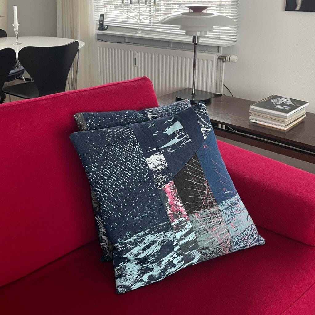 View of two Space Collection large pillows by MIN-studio on a red sofa. The pillows are screen-printed denim with layered moon surface textures in blue, grey, and neon pink inks, featuring edgy, grunge-inspired abstract patterns.